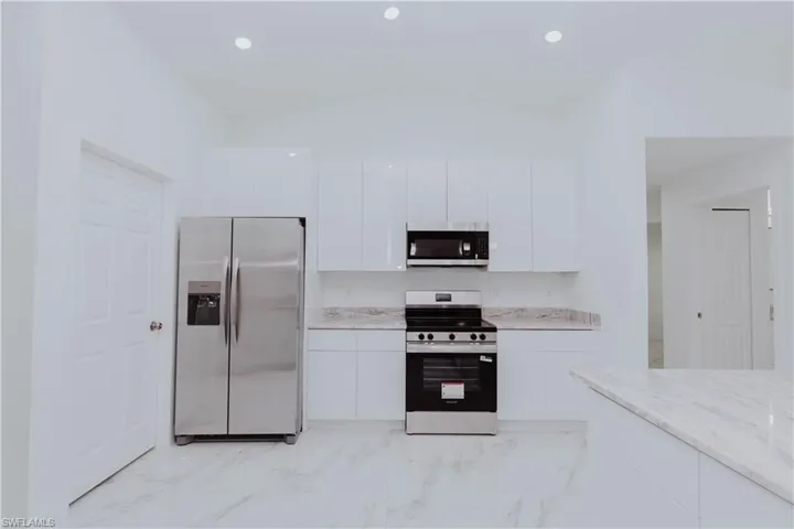 Kitchen with a peninsula, appliances with stainless steel finishes, pendant lighting, light marble finish flooring, and recessed lighting