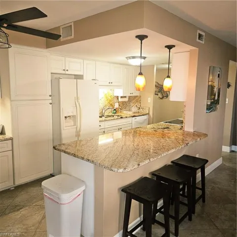 Kitchen with a kitchen bar, refrigerator, hanging light fixtures, a peninsula, and backsplash