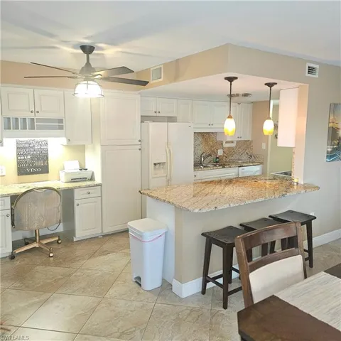 Kitchen featuring a kitchen bar, hanging light fixtures, white cabinets, and light stone countertops