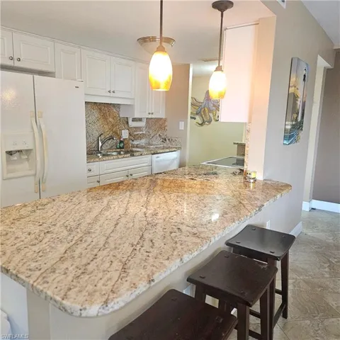 Kitchen featuring a breakfast bar area, white appliances, backsplash, light stone countertops, and a peninsula