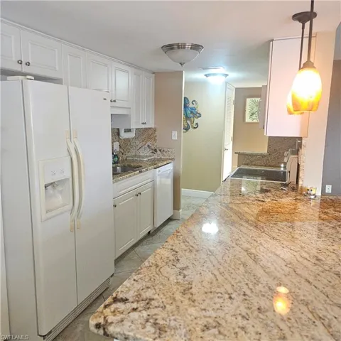 Kitchen featuring white appliances, light stone countertops, white cabinetry, backsplash, and decorative light fixtures