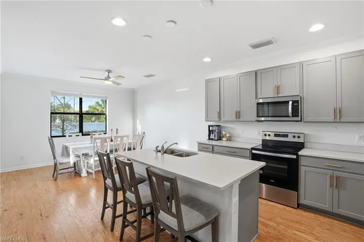 Kitchen featuring gray cabinetry, stainless steel appliances, crown molding, a center island with sink, and light wood-type flooring