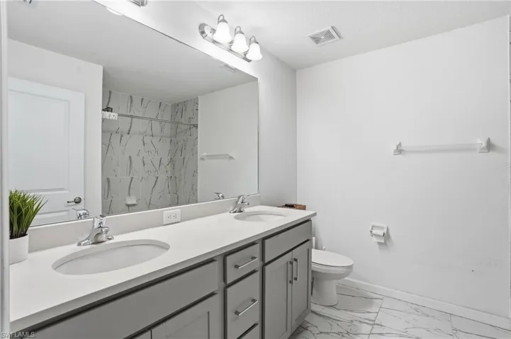 Bathroom with double vanity, light marble finish flooring, and a shower