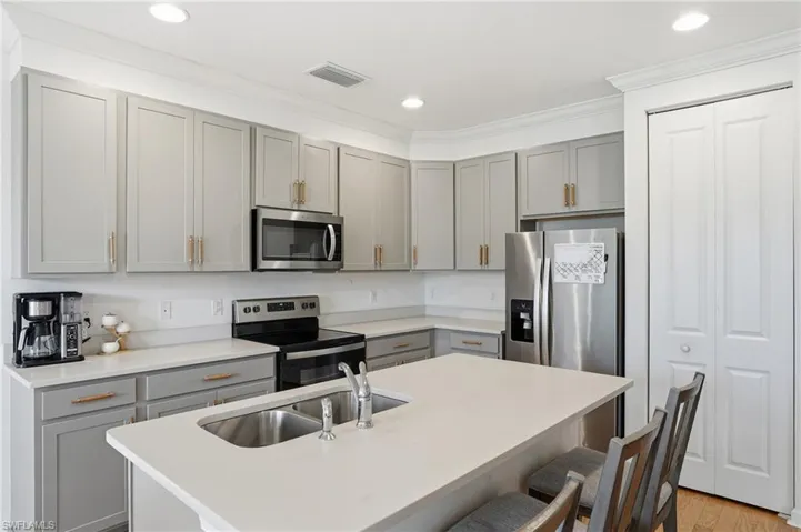 Kitchen with gray cabinetry, stainless steel appliances, a center island with sink, a kitchen bar, and recessed lighting