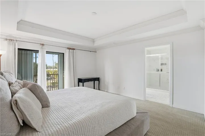 Carpeted bedroom featuring access to outside, a tray ceiling, connected bathroom, and crown molding