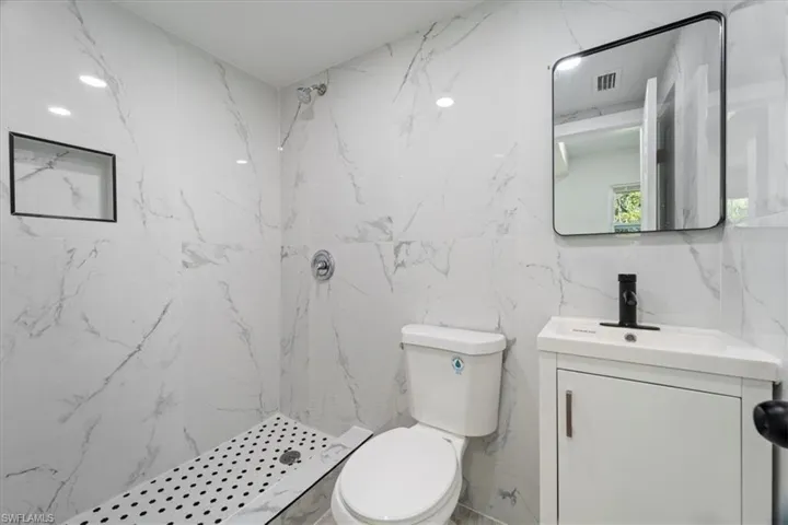 Full bathroom featuring visible vents, a marble finish shower, toilet, tile walls, and vanity