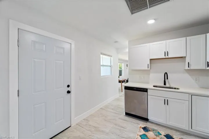 Kitchen featuring stainless steel dishwasher, light countertops, a sink, white cabinetry, and visible vents