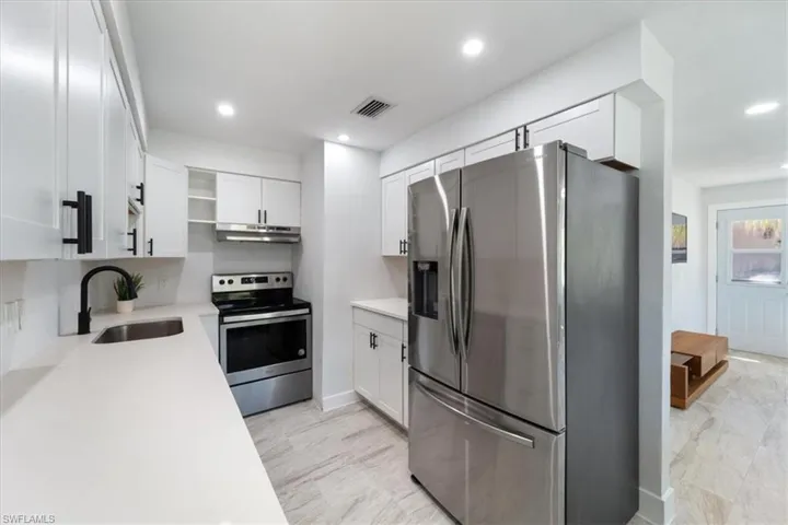 Kitchen featuring a sink, appliances with stainless steel finishes, under cabinet range hood, and light countertops