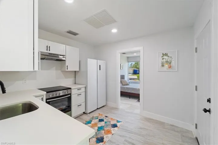 Kitchen featuring a sink, under cabinet range hood, stainless steel electric range, visible vents, and freestanding refrigerator
