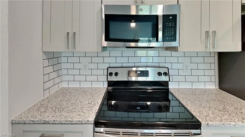 Kitchen with stainless steel appliances, light stone countertops, white cabinets, and decorative backsplash