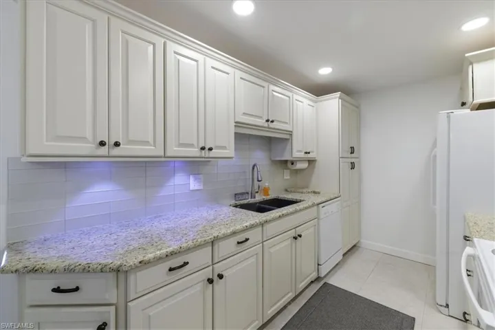 Kitchen with white cabinets, white appliances, light stone counters, and recessed lighting