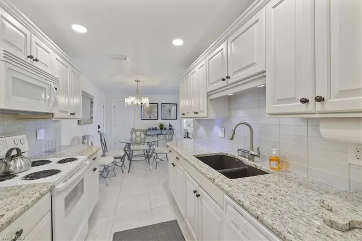 Kitchen with white appliances, white cabinetry, a chandelier, and light stone countertops