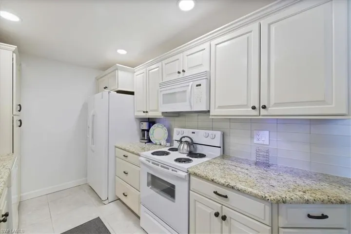 Kitchen featuring white appliances, white cabinetry, tasteful backsplash, light tile patterned floors, and recessed lighting