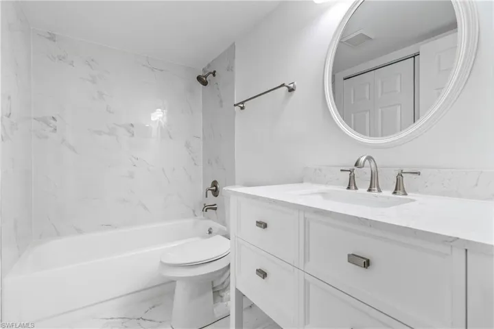 Bathroom featuring bathtub / shower combination, vanity, and light marble finish floors