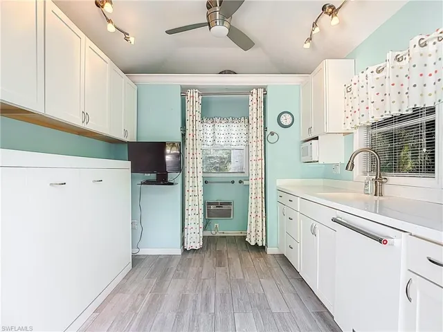 Kitchen featuring white cabinets, rail lighting, a ceiling fan, white dishwasher, and vaulted ceiling