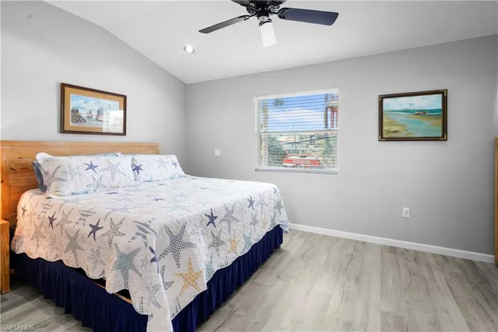 Bedroom featuring light wood finished floors, vaulted ceiling, baseboards, and a ceiling fan