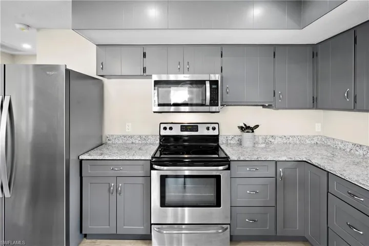 Kitchen with appliances with stainless steel finishes, gray cabinetry, and light stone counters