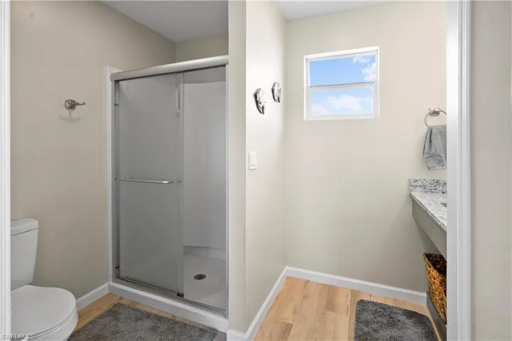 Full bath with wood finished floors, toilet, baseboards, and a stall shower