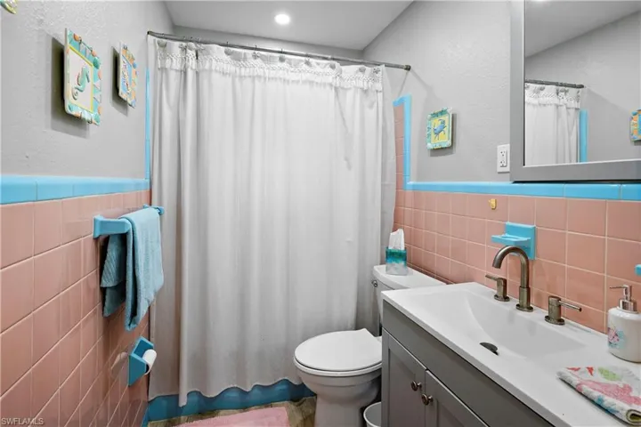 Full bathroom featuring tile walls, toilet, vanity, a wainscoted wall, and a shower with shower curtain