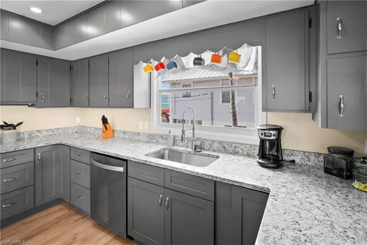 Kitchen with stainless steel dishwasher, a sink, gray cabinetry, light wood finished floors, and light stone countertops