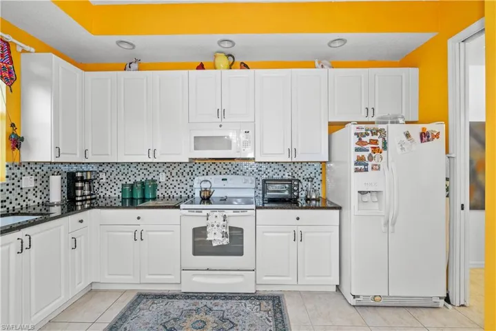 Kitchen with white appliances, white cabinetry, dark stone counters, decorative backsplash, and light tile patterned flooring