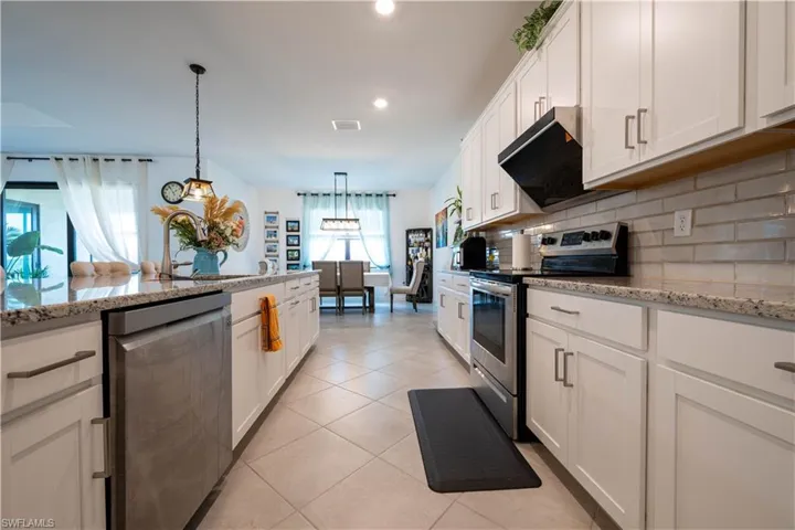 Kitchen with appliances with stainless steel finishes, white cabinetry, light stone counters, decorative backsplash, and light tile patterned floors