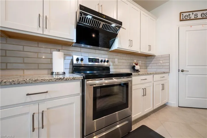 Kitchen with stainless steel range with electric cooktop, white cabinets, light stone countertops, tasteful backsplash, and light tile patterned flooring