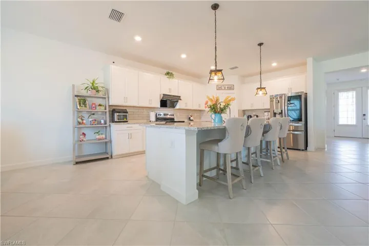 Kitchen featuring stainless steel appliances, a breakfast bar area, a center island with sink, white cabinetry, and recessed lighting