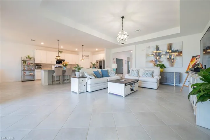 Living room featuring a tray ceiling, a chandelier, light tile patterned flooring, and recessed lighting