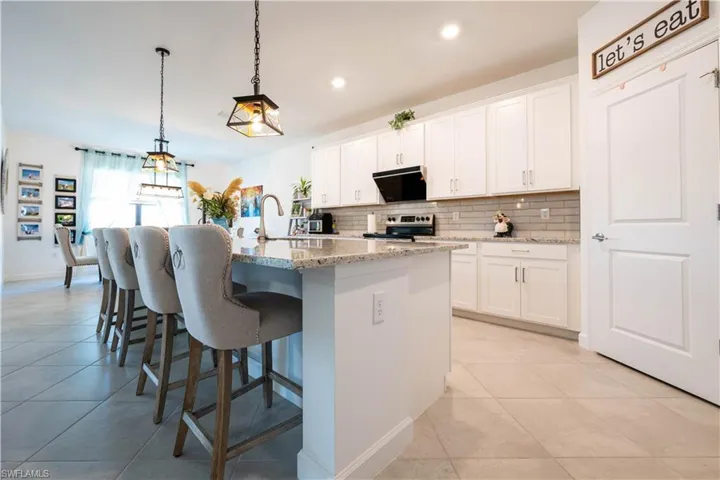 Kitchen featuring light tile patterned flooring, a breakfast bar area, light stone counters, an island with sink, and white cabinetry