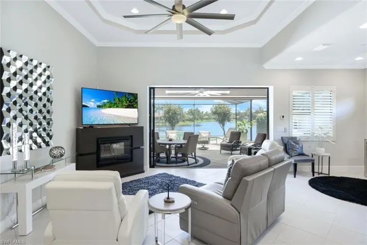 Tiled living room featuring ceiling fan, a tray ceiling, and ornamental molding