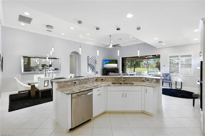 Kitchen with pendant lighting, light stone counters, stainless steel dishwasher, an island with sink, and white cabinetry