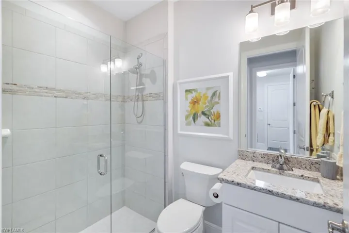 Bathroom featuring a shower with door, toilet, and vanity