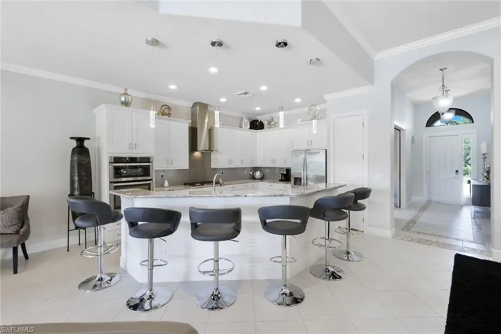 Kitchen with stainless steel appliances, decorative light fixtures, a kitchen island with sink, and wall chimney range hood