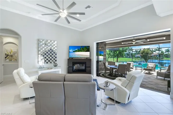 Living room with light tile patterned flooring, a water view, ceiling fan, and a raised ceiling