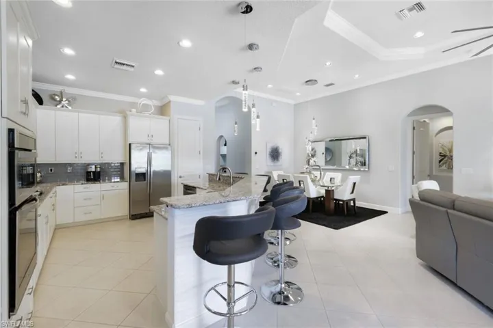 Kitchen featuring white cabinetry, stainless steel appliances, light stone countertops, and ornamental molding