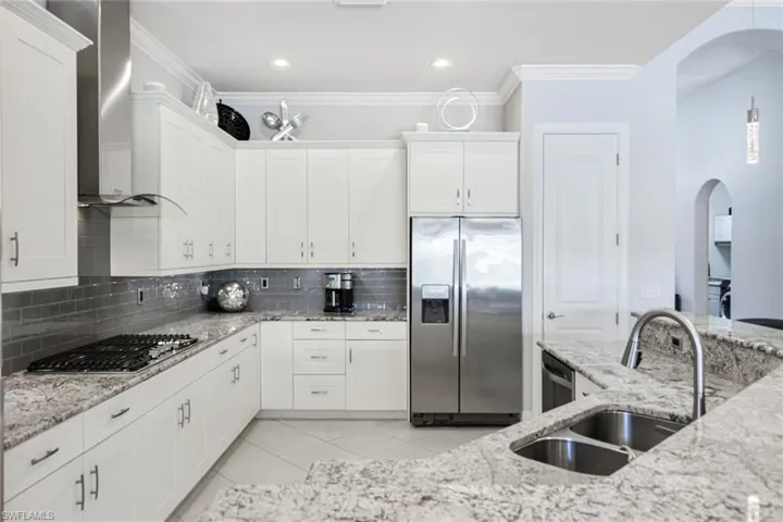 Kitchen featuring light tile patterned floors, wall chimney range hood, stainless steel appliances, decorative backsplash, and sink