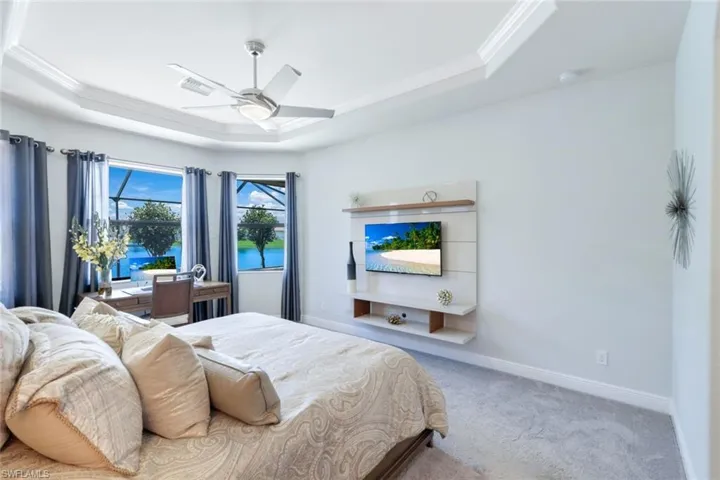 Carpeted bedroom with ceiling fan, ornamental molding, and a tray ceiling