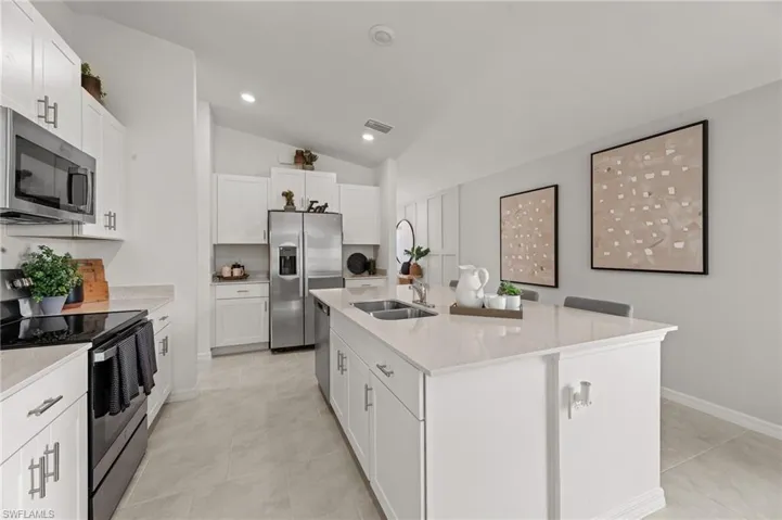 Kitchen with appliances with stainless steel finishes, lofted ceiling, an island with sink, light stone countertops, and white cabinets