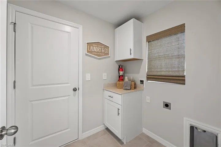 Washroom with light tile patterned floors, washer hookup, cabinet space, and hookup for an electric dryer