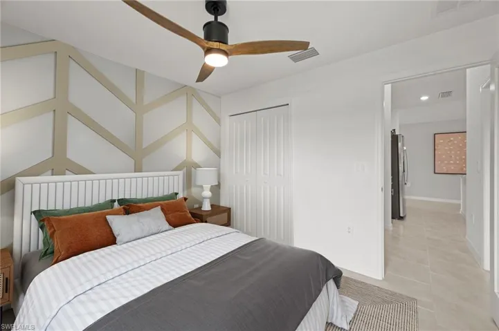 Bedroom with light tile patterned floors, freestanding refrigerator, ceiling fan, and a closet
