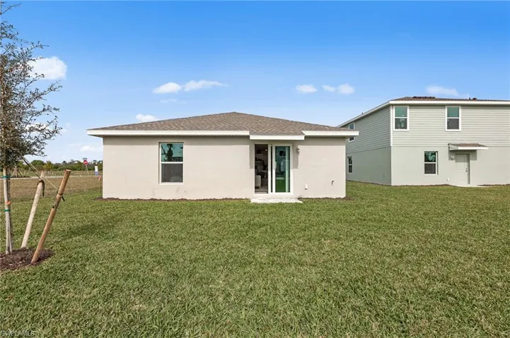 Back of property with stucco siding, a yard, and roof with shingles