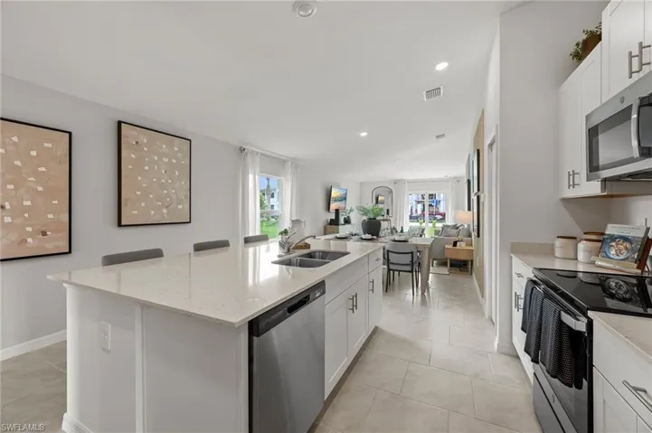 Kitchen featuring white cabinets, stainless steel appliances, light stone countertops, open floor plan, and a kitchen island with sink