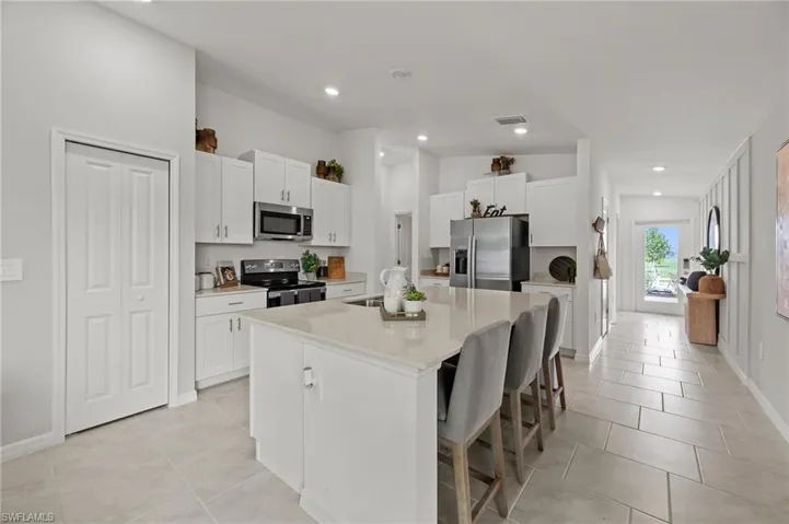 Kitchen with appliances with stainless steel finishes, a kitchen bar, an island with sink, white cabinetry, and light stone counters