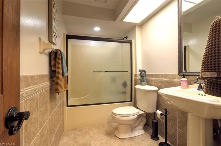 Bathroom with tile flooring, enclosed tub / shower combo, toilet, and tile walls