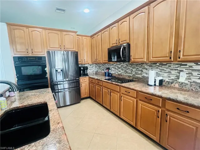 Kitchen featuring backsplash, black appliances, light stone counters, and light tile patterned floors