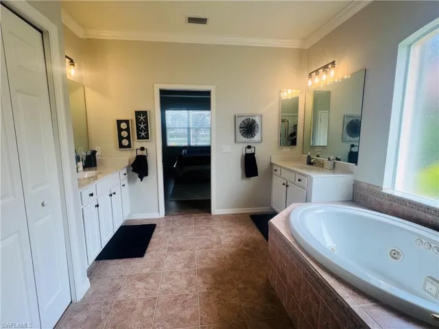 Bathroom featuring tiled tub, vanity, tile patterned floors, and crown molding