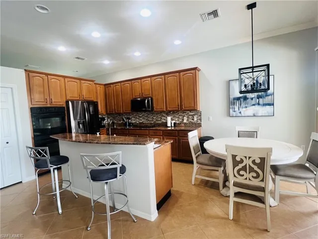 Kitchen featuring appliances with stainless steel finishes, dark stone counters, tasteful backsplash, a center island with sink, and hanging light fixtures