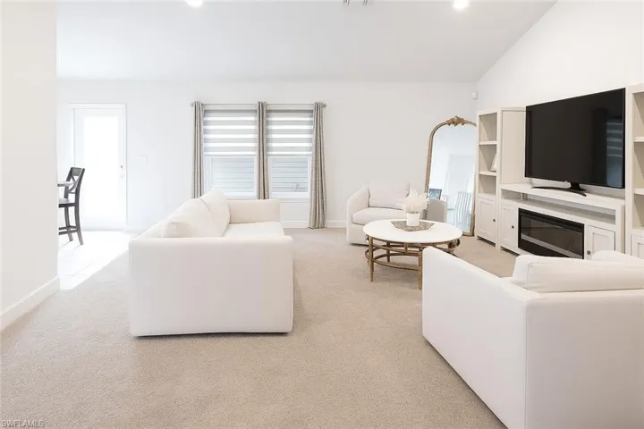 Living area with lofted ceiling, light colored carpet, a glass covered fireplace, recessed lighting, and arched walkways