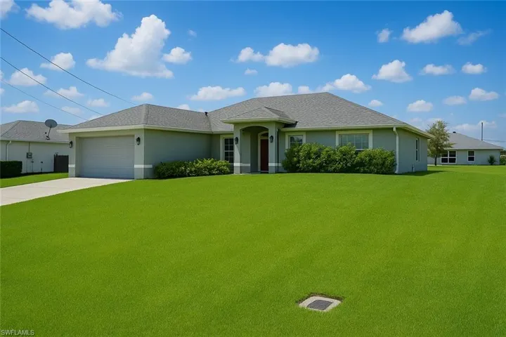 Ranch-style home with a front yard, stucco siding, concrete driveway, and a garage